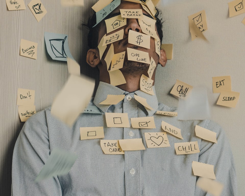 A man at a desk covered in sticky notes reading 'take a break', 'stop' and 'chill'